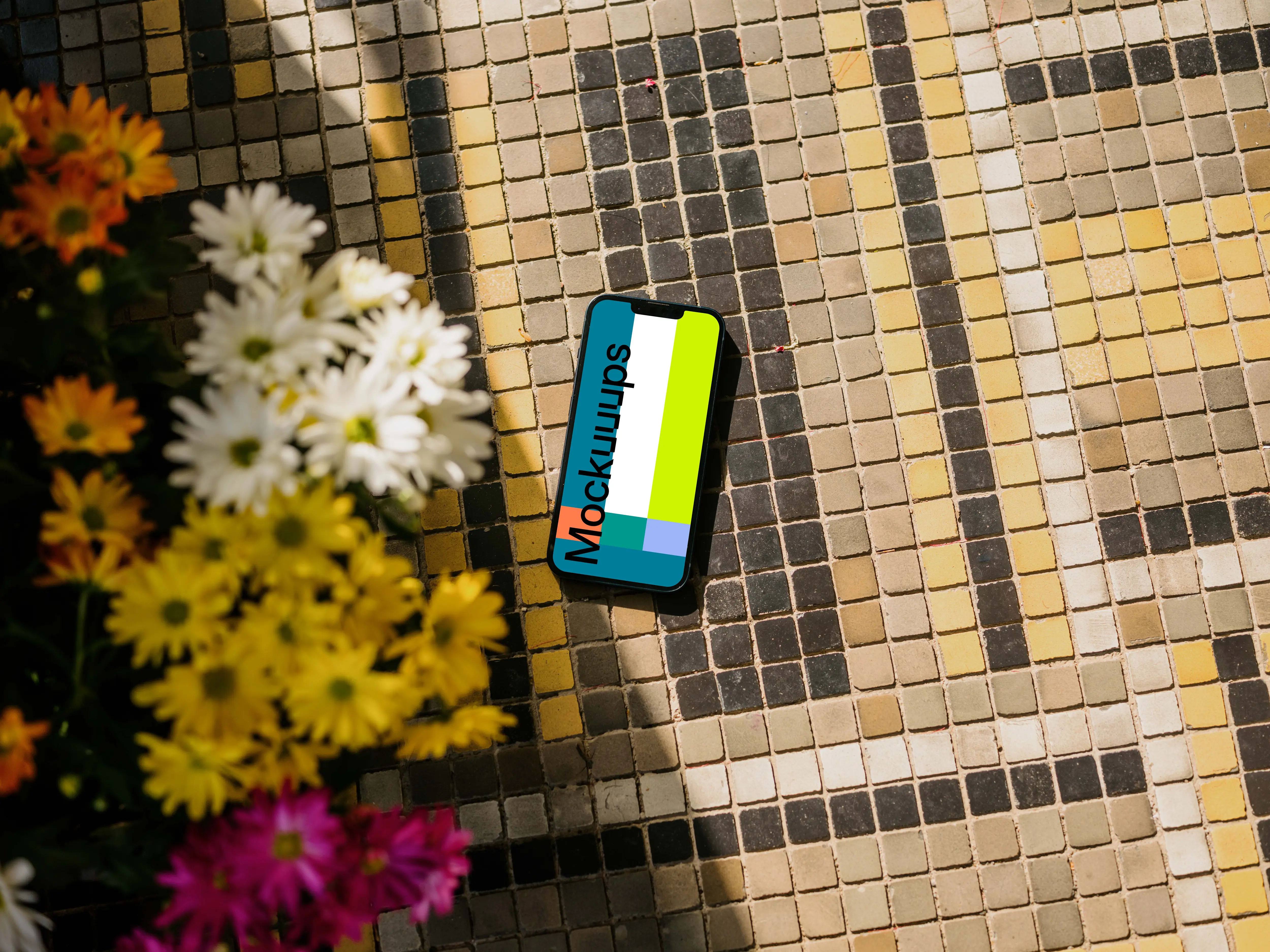 iPhone 13 mockup on a garden paving next to the flowers