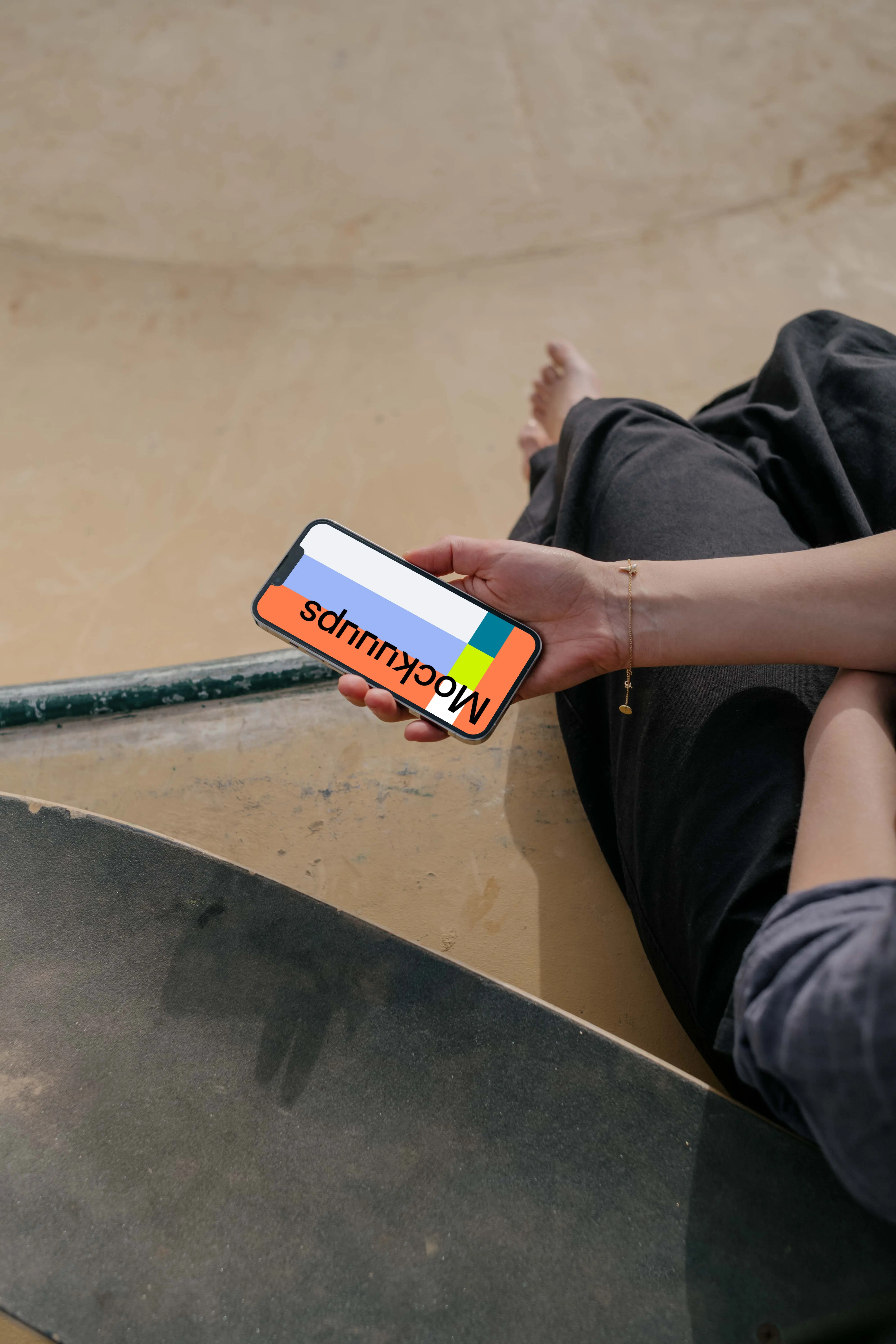  iPhone 13 Pro mockup held by a user seated next to a skateboard