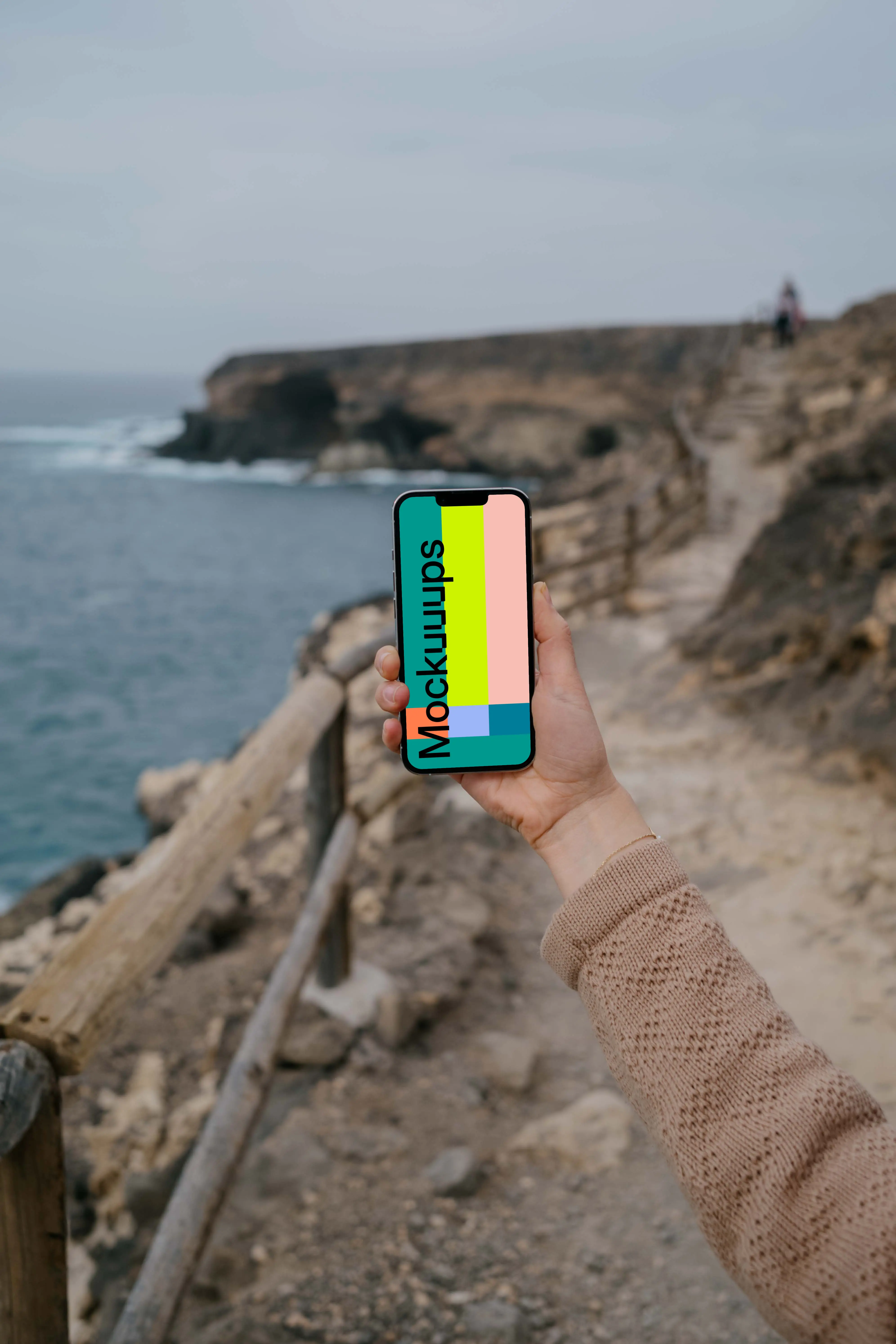 iPhone 13 Pro mockup held up beside the ocean