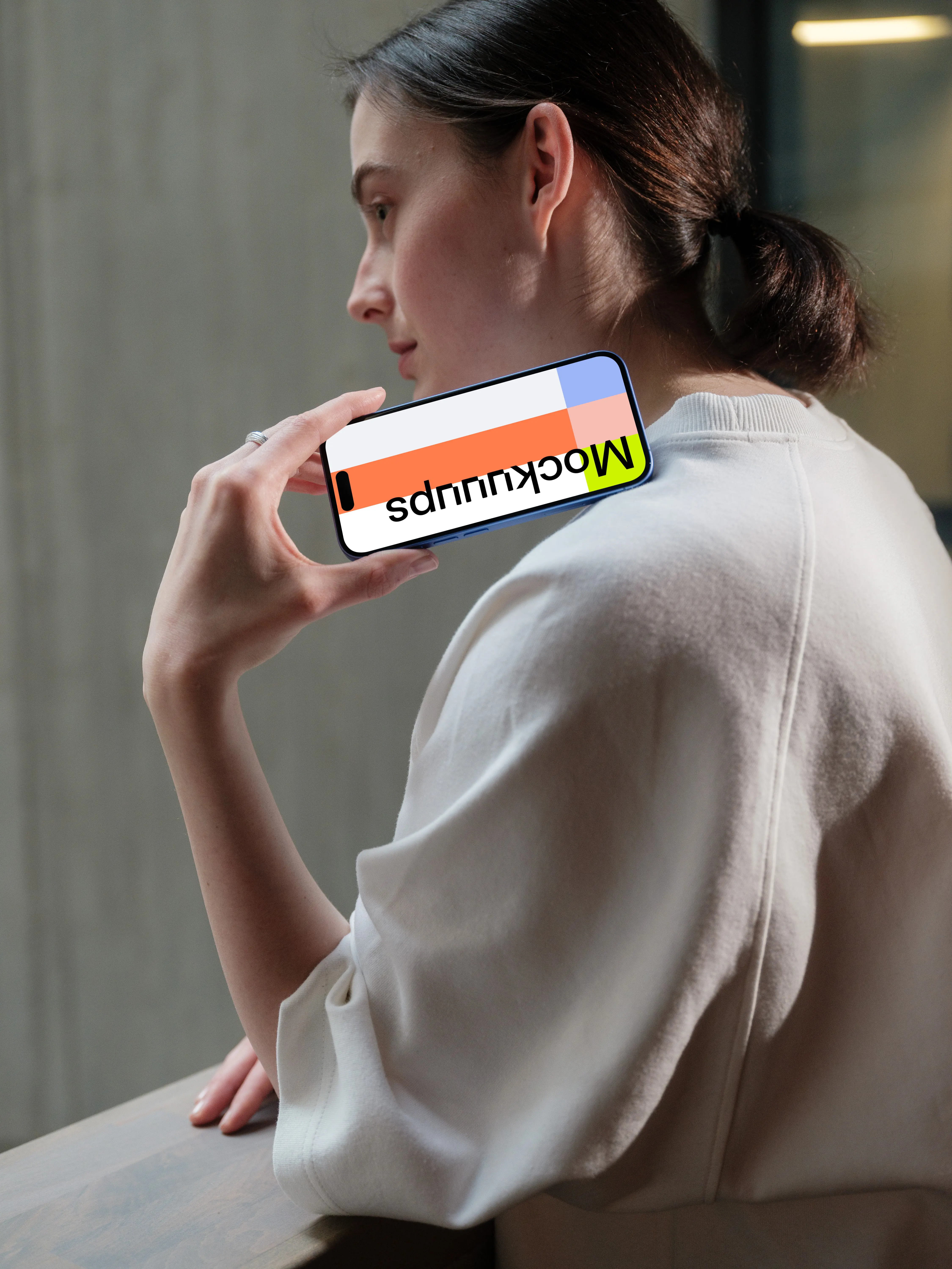 iPhone 16 mockup held by woman near concrete wall