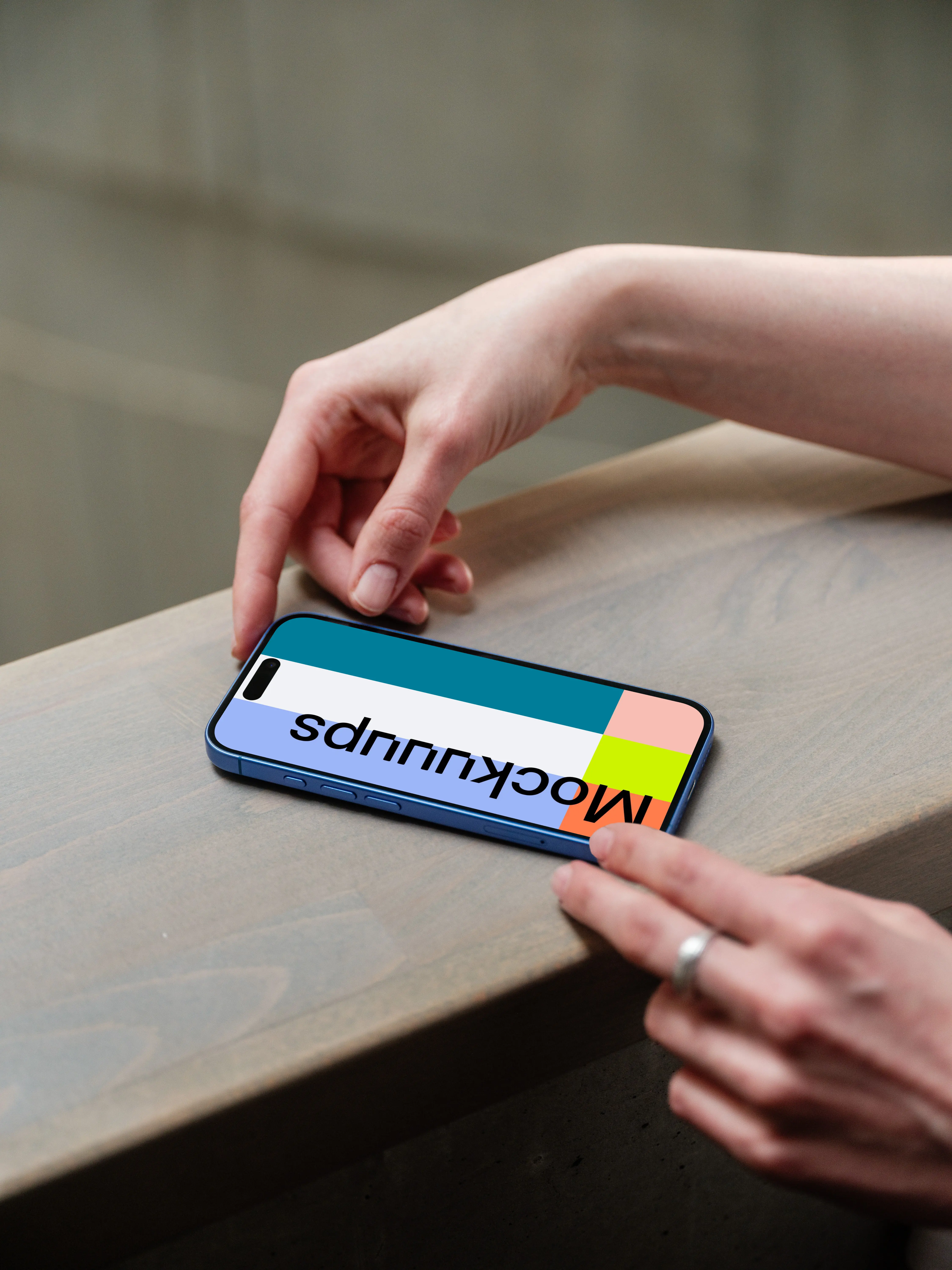 iPhone 16 mockup on a wooden surface with a hand interacting