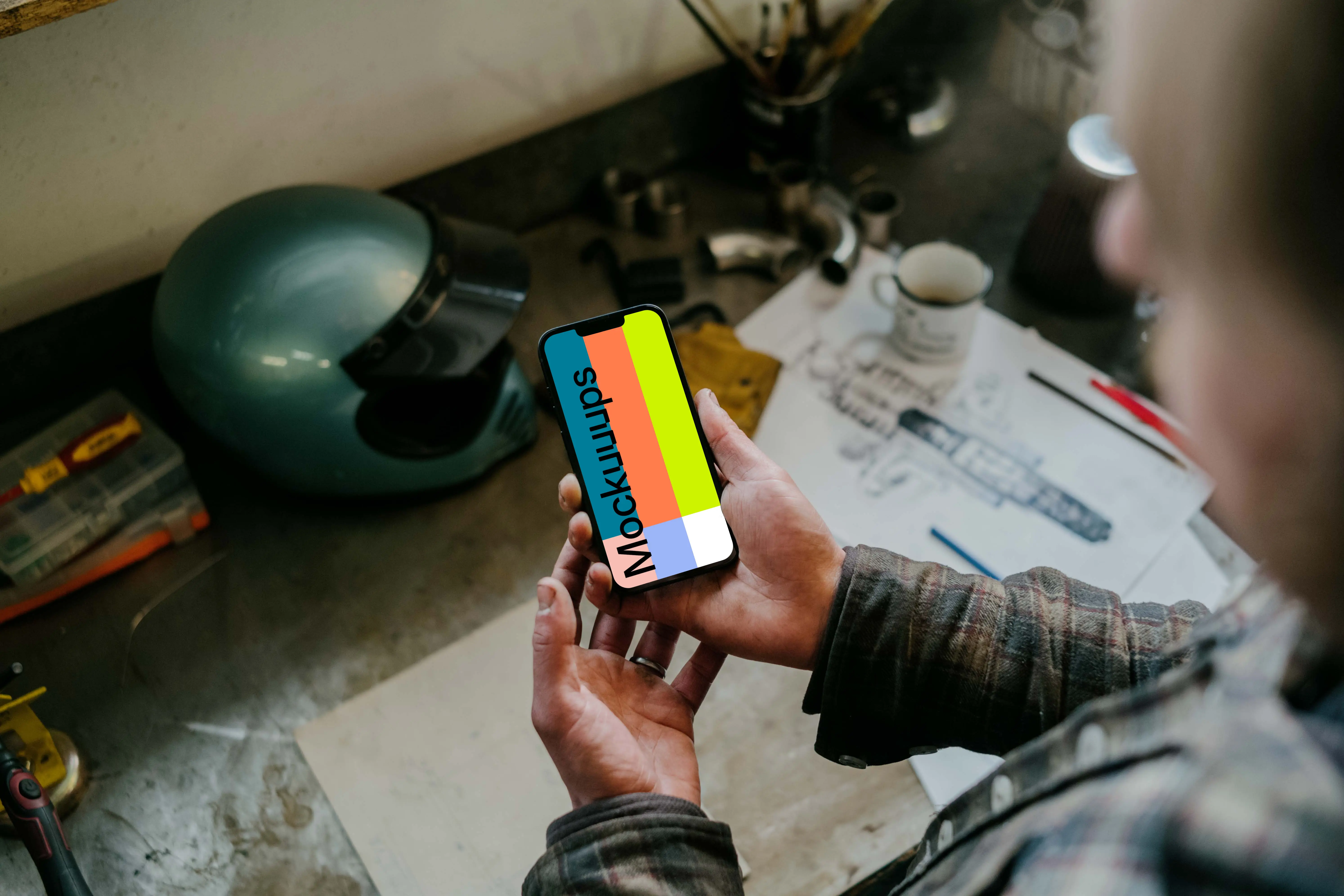 Man holding an iPhone 13 Pro mockup over a mechanic work table