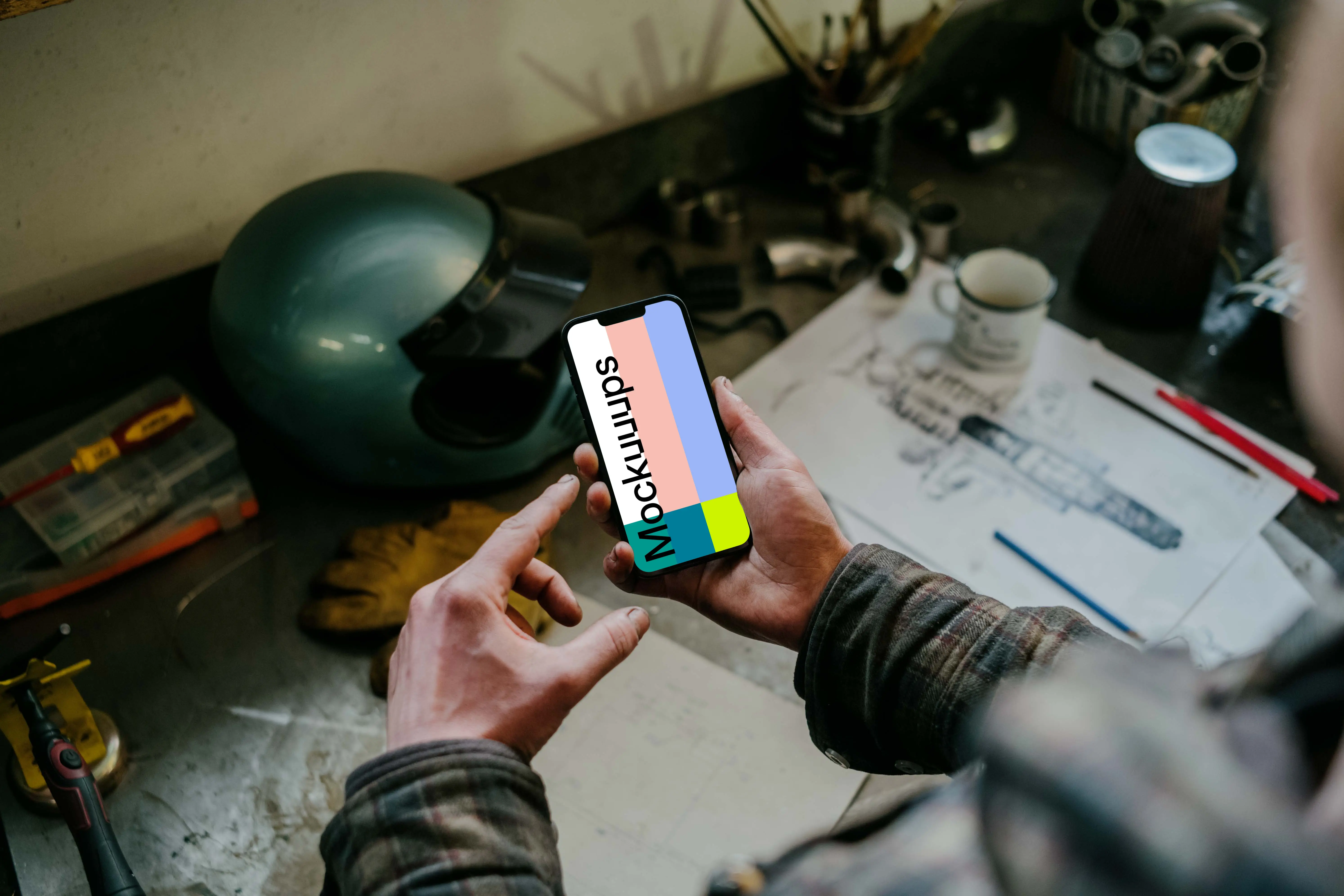 Man holding an iPhone 13 Pro mockup over a mechanic’s table