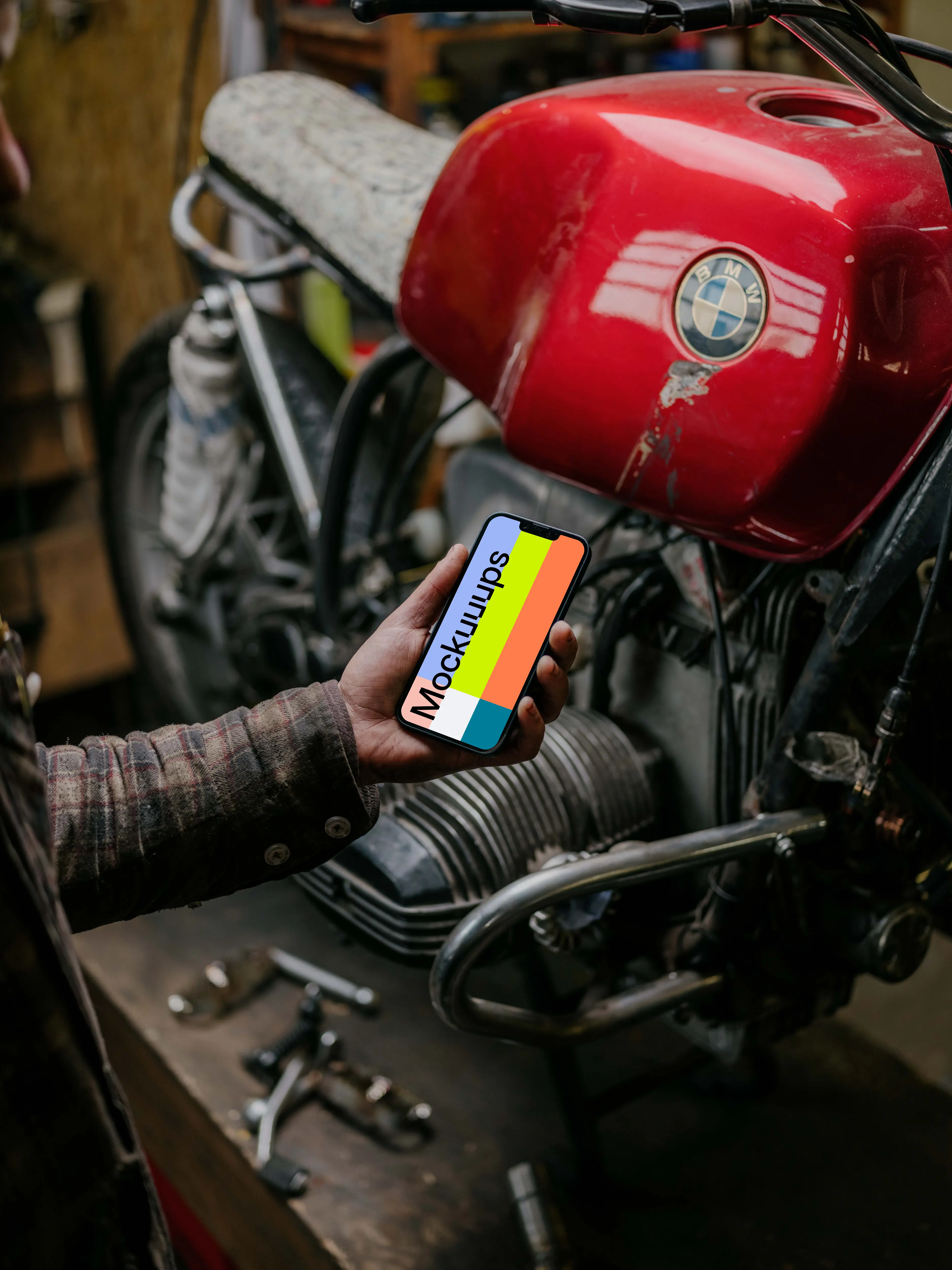 Man holding up an iPhone 13 Pro mockup beside a motorcycle