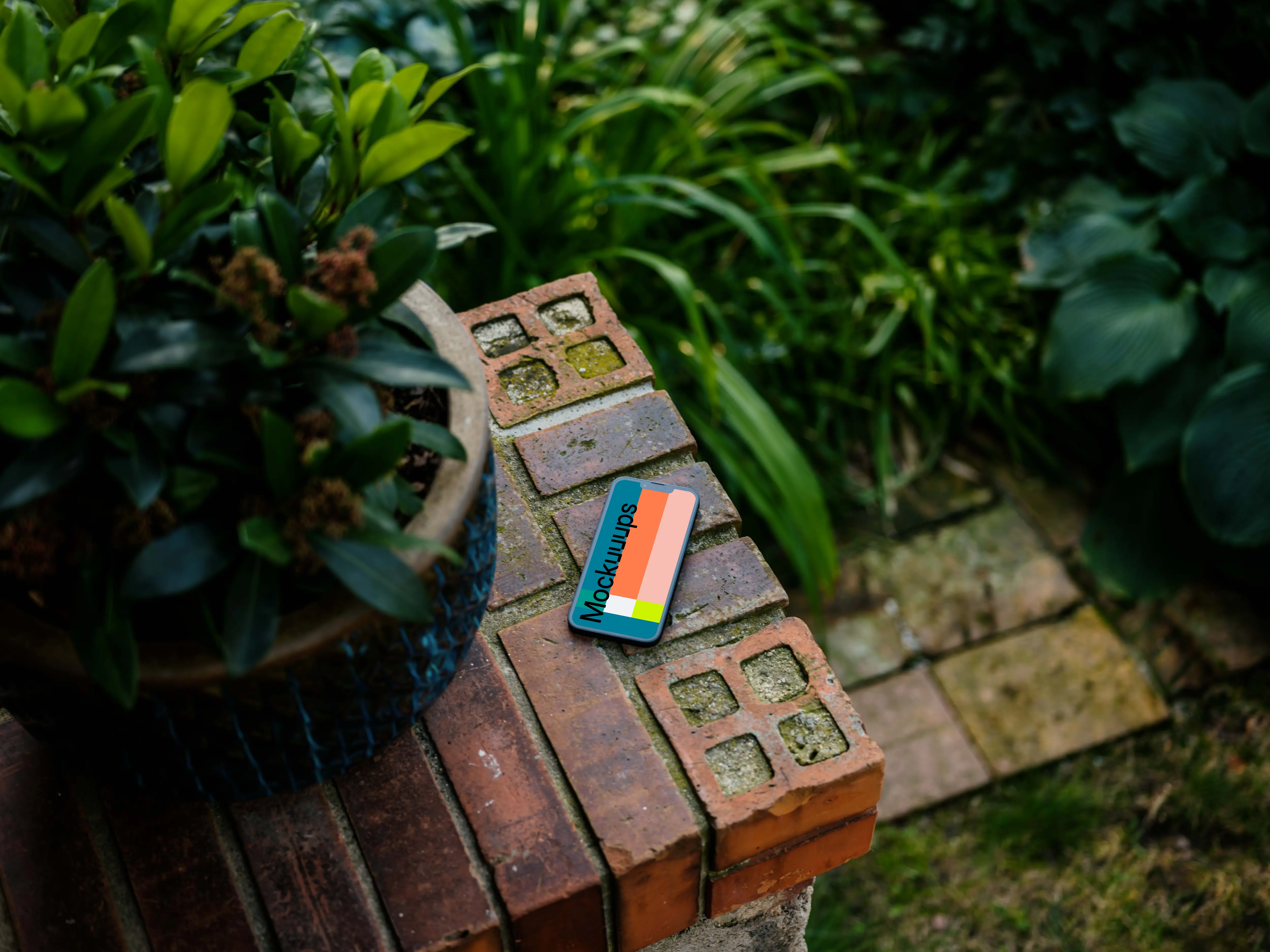 Phone mockup on a stone wall with plants in the background