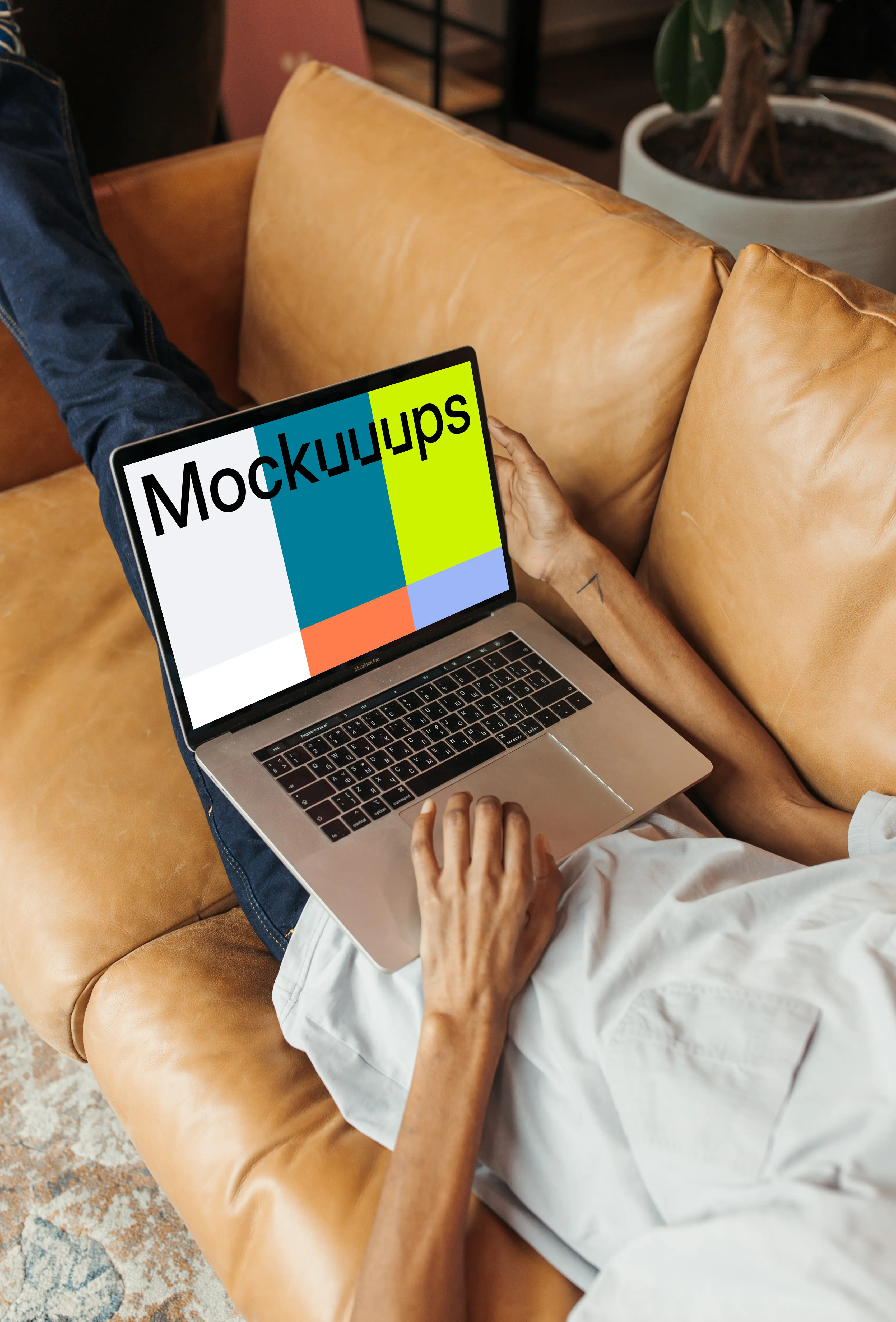 User on a leather sofa holding a MacBook Pro mockup