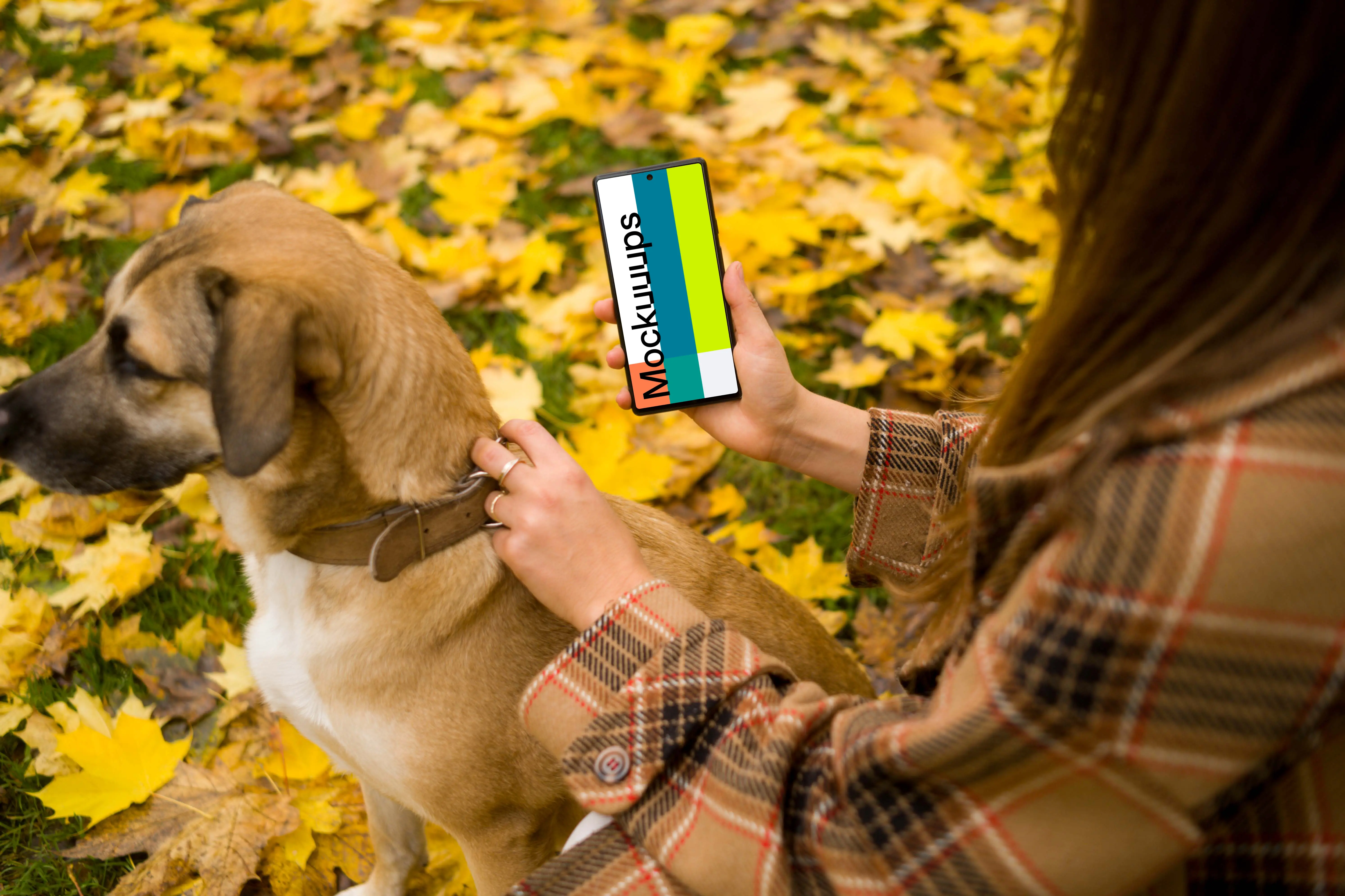 Woman holding a phone and dog in autumn themed park mockup