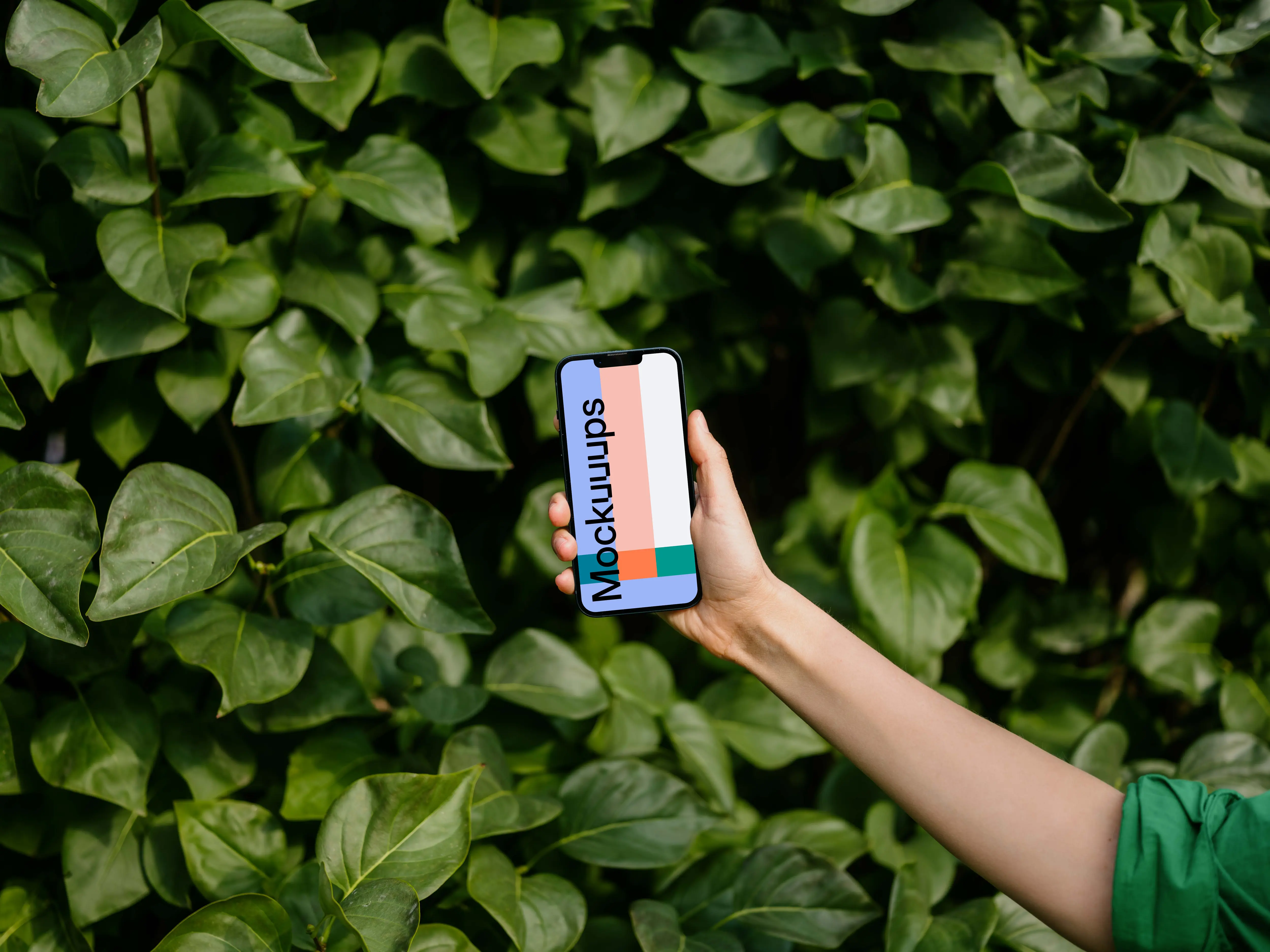 Woman holding an iPhone 13 mockup in front of green leaves