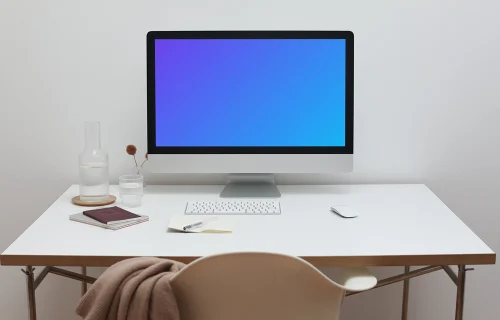 iMac mockup on a table with a jacket hanging on a chair in front of it