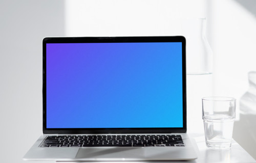 MacBook mockup on a white table with glass of water at the side