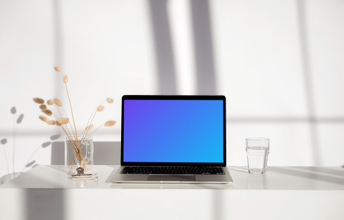 MacBook mockup on a white table with glass of water next to it
