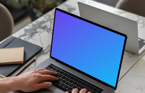 MacBook Pro mockup on a white table beside a notebook