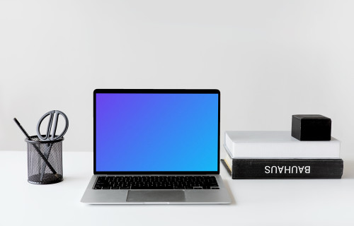 Black MacBook mockup on a white table with black textbooks at the side