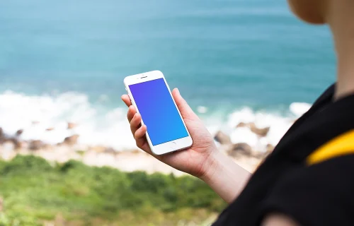 Holding iPhone 7 mockup next to the ocean