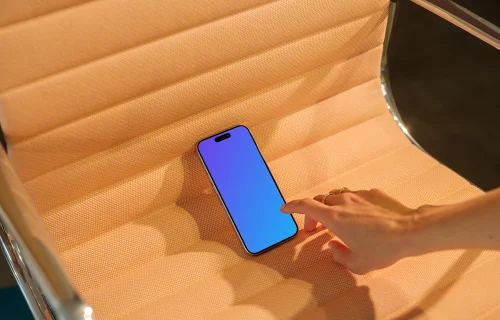 iPhone 15 Pro mockup on a textured orange seat with a hand interacting