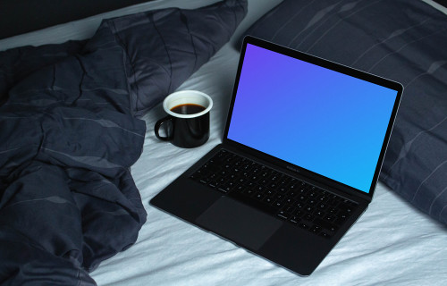 MacBook mockup em uma cama branca ao lado de uma xícara de café e um edredom azul 