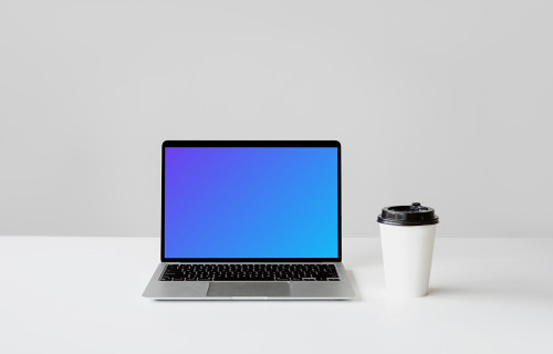 MacBook mockup on a white table with a disposable coffee cup at the side