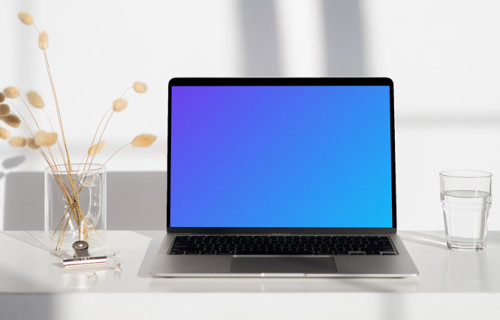 MacBook mockup on a white table with a glass of water at the side