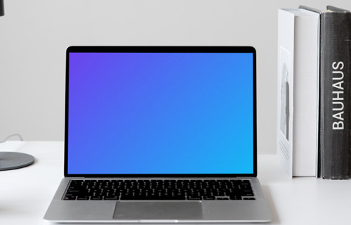 MacBook mockup on a white table with books stacked vertically at the side