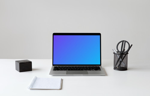 MacBook mockup on a white workstation table with cup of pens and scissors at the side