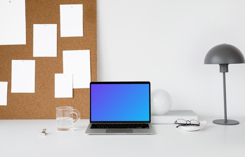 MacBook mockup on a white workstation table with task board at the side