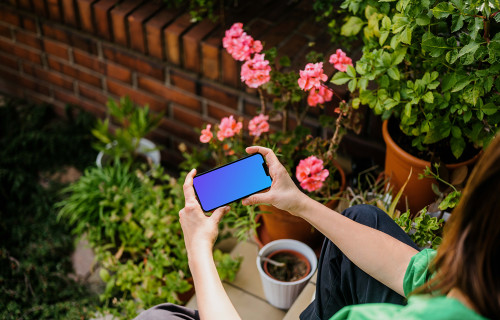 Mulher sentada em um jardim segurando um iPhone 13 mockup