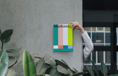 A4 mockup held against a concrete wall with indoor plants