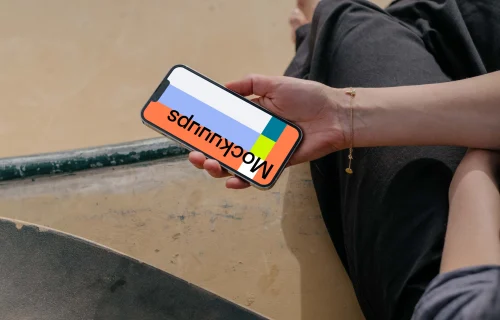  iPhone 13 Pro mockup held by a user seated next to a skateboard