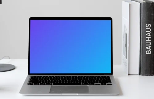 MacBook mockup on a white table with books stacked vertically at the side