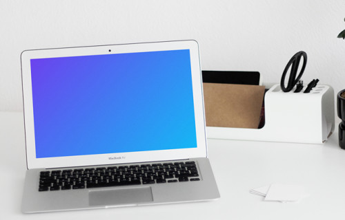 MacBook mockup on a white table with writing materials on the side