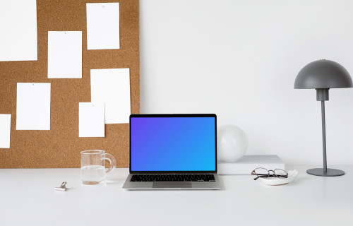 MacBook mockup on a white workstation table with task board at the side