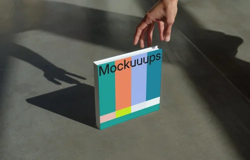 Mockup of a square book on a concrete surface with a hand reaching