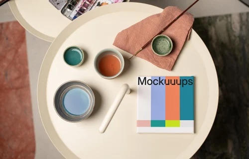 Mockup of a square poster with art supplies on a round table