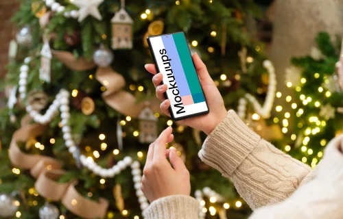 Woman hand holding a smartphone next to the Christmas tree