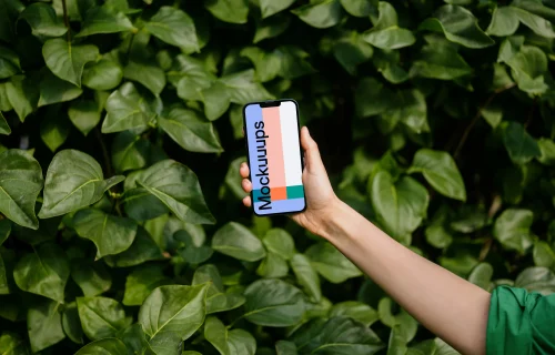 Woman holding an iPhone 13 mockup in front of green leaves