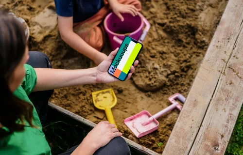 Woman holding an iPhone 13 mockup in sandpit