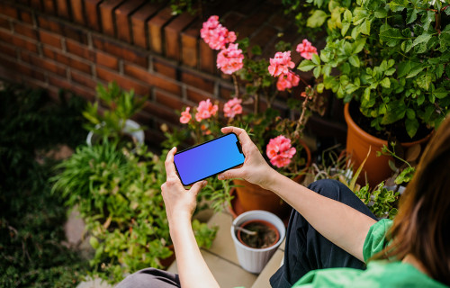 Woman sitting in garden while holding an iPhone 13 mockup
