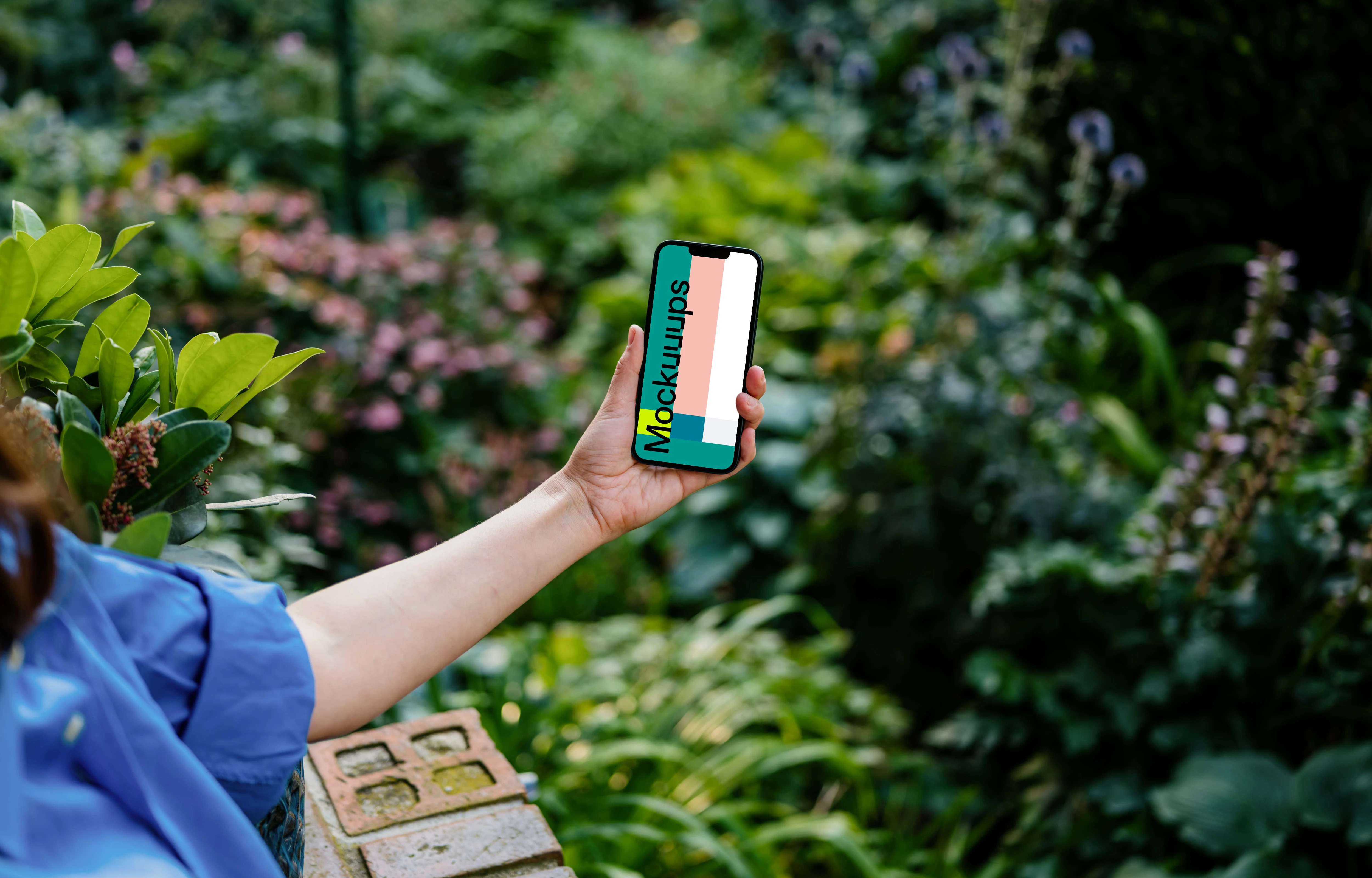 Hand holding an iPhone 13 mockup surrounded by plants