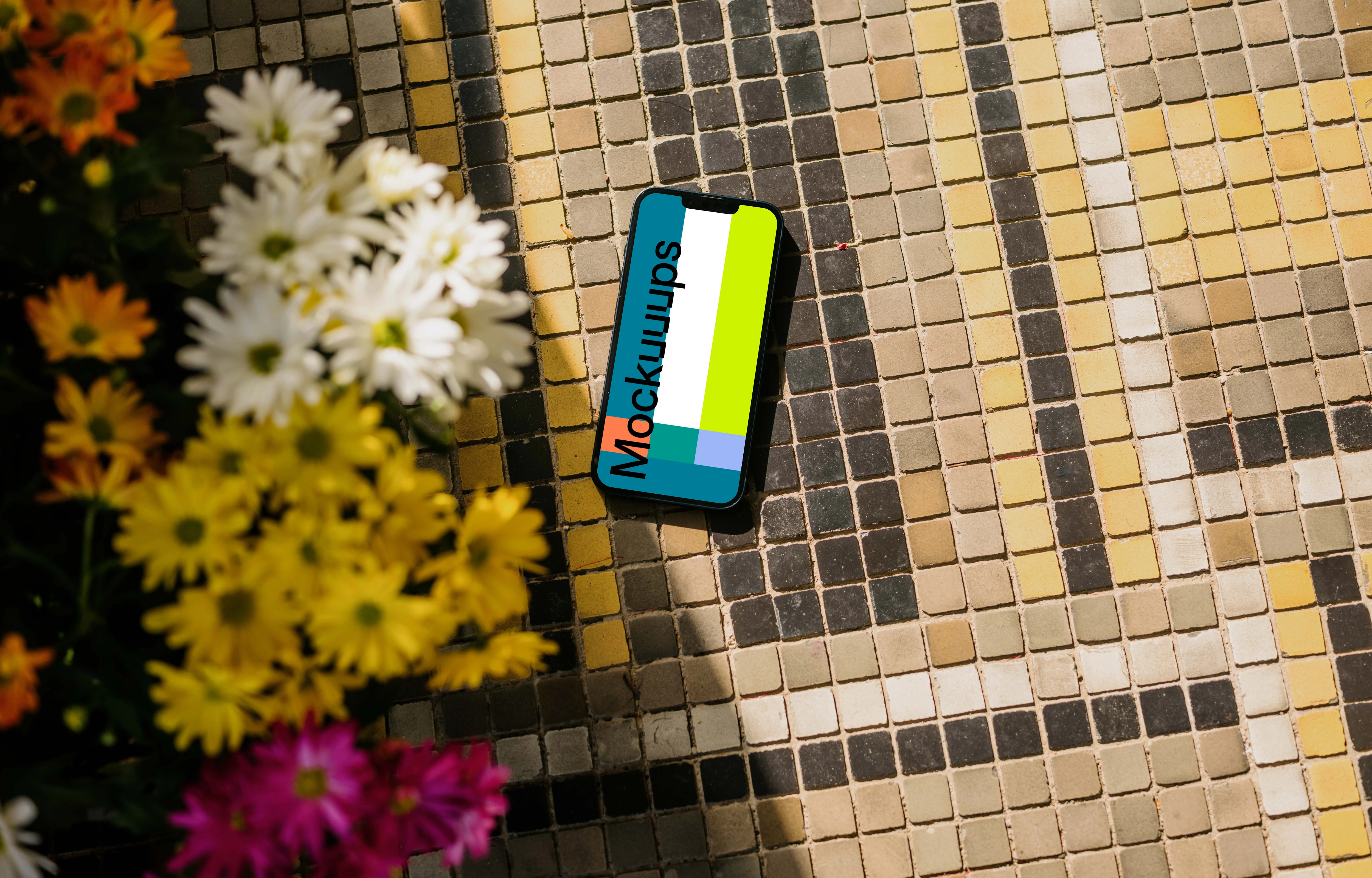 iPhone 13 mockup on a garden paving next to the flowers
