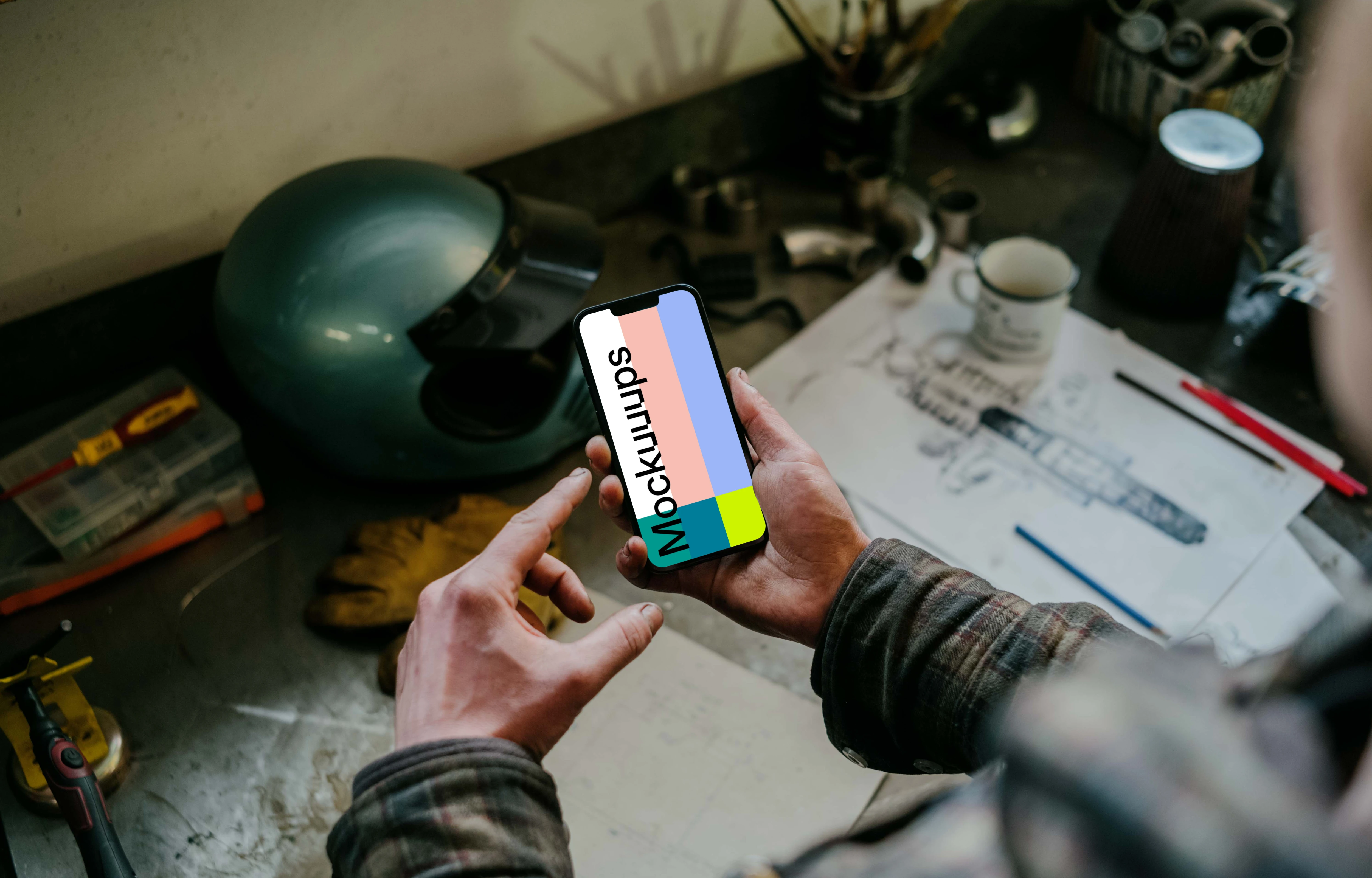 Man holding an iPhone 13 Pro mockup over a mechanic’s table