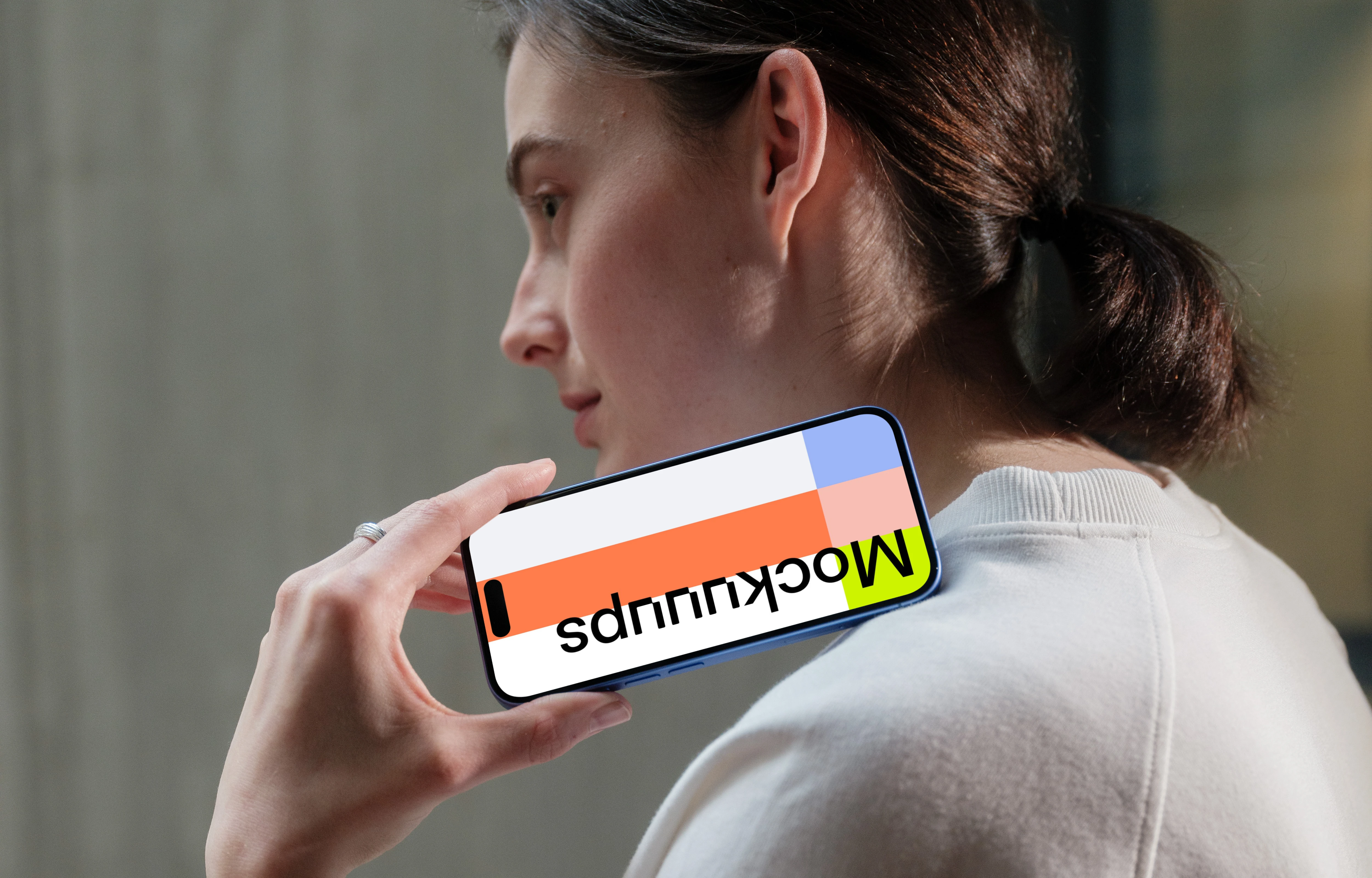 iPhone 16 mockup held by woman near concrete wall