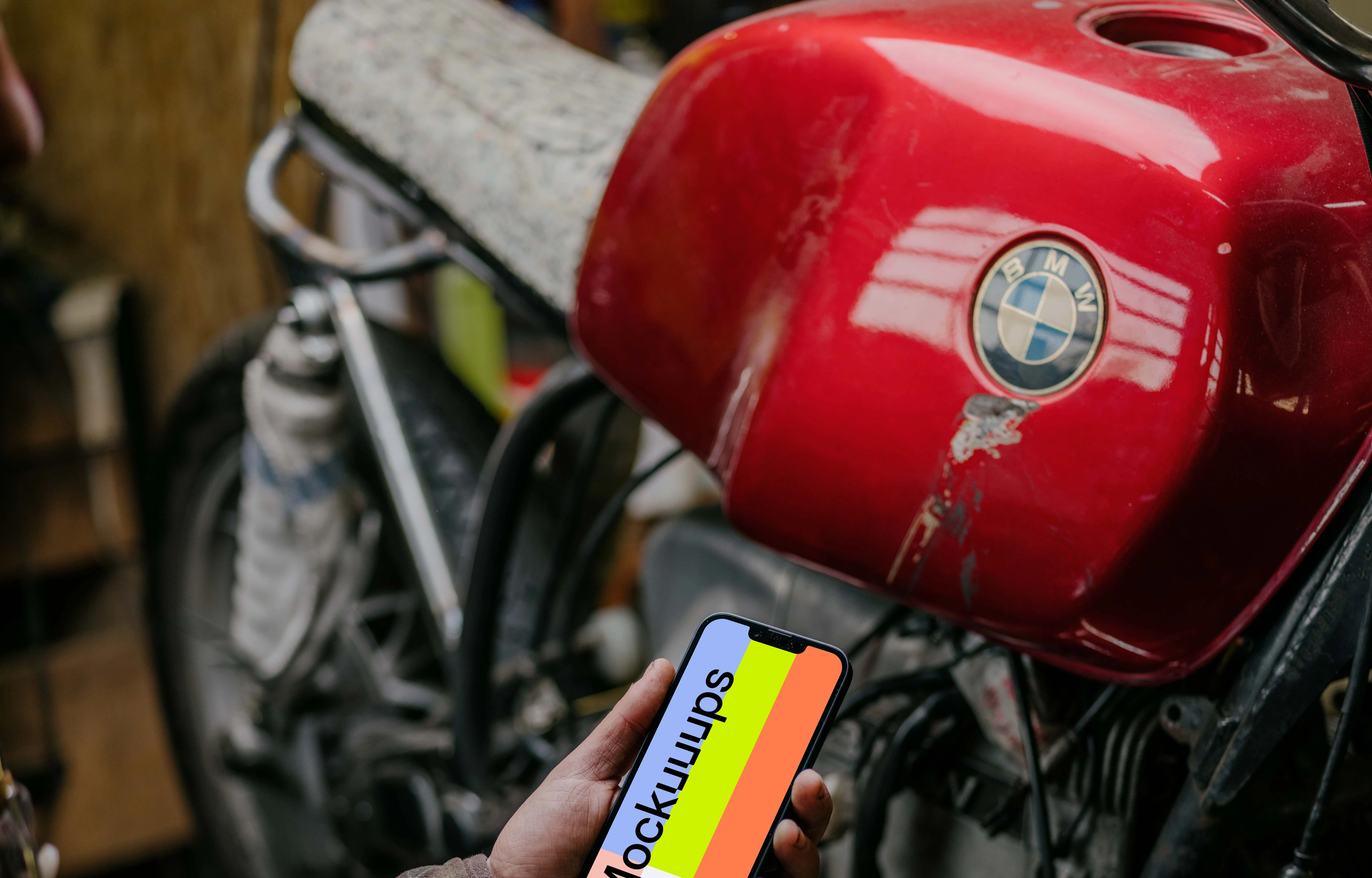 Man holding up an iPhone 13 Pro mockup beside a motorcycle