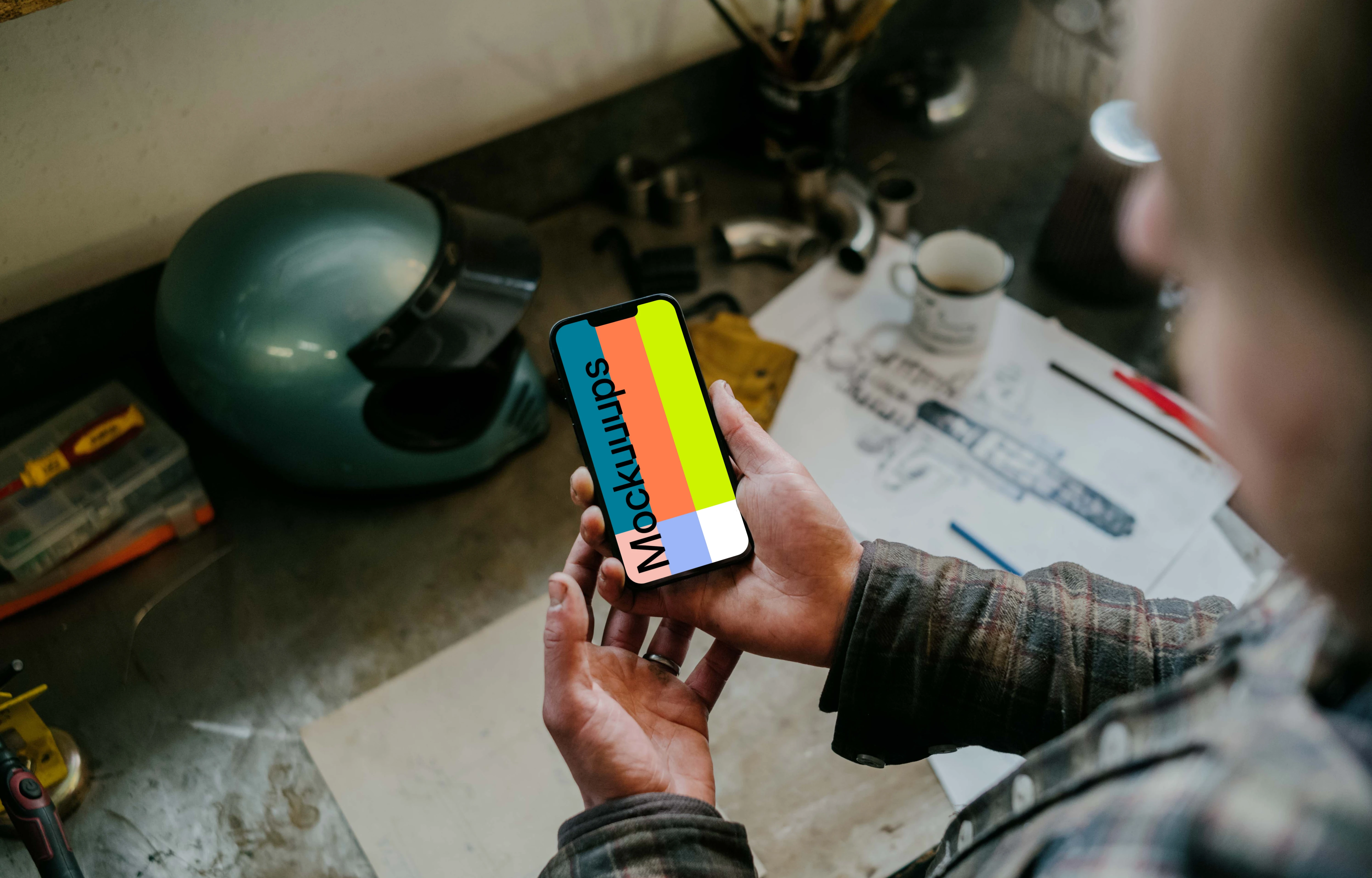 Man holding an iPhone 13 Pro mockup over a mechanic work table
