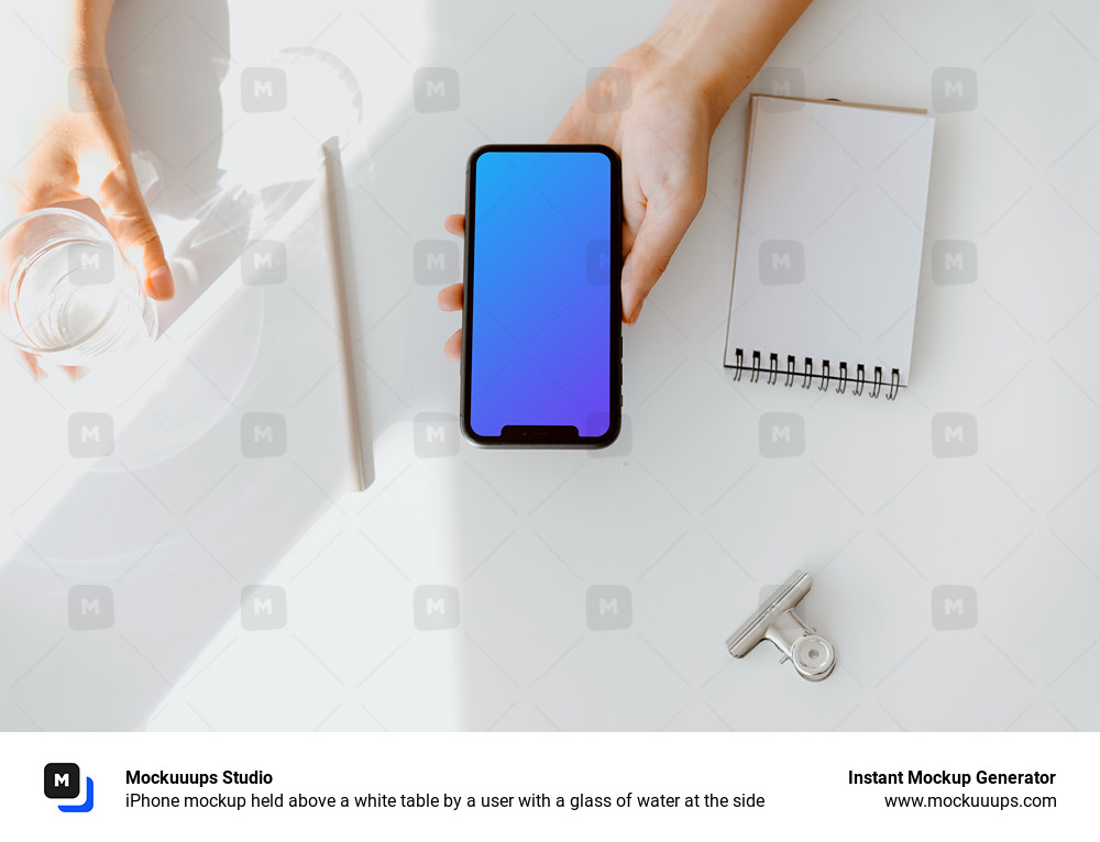 iPhone mockup held above a white table by a user with a glass of water at the side