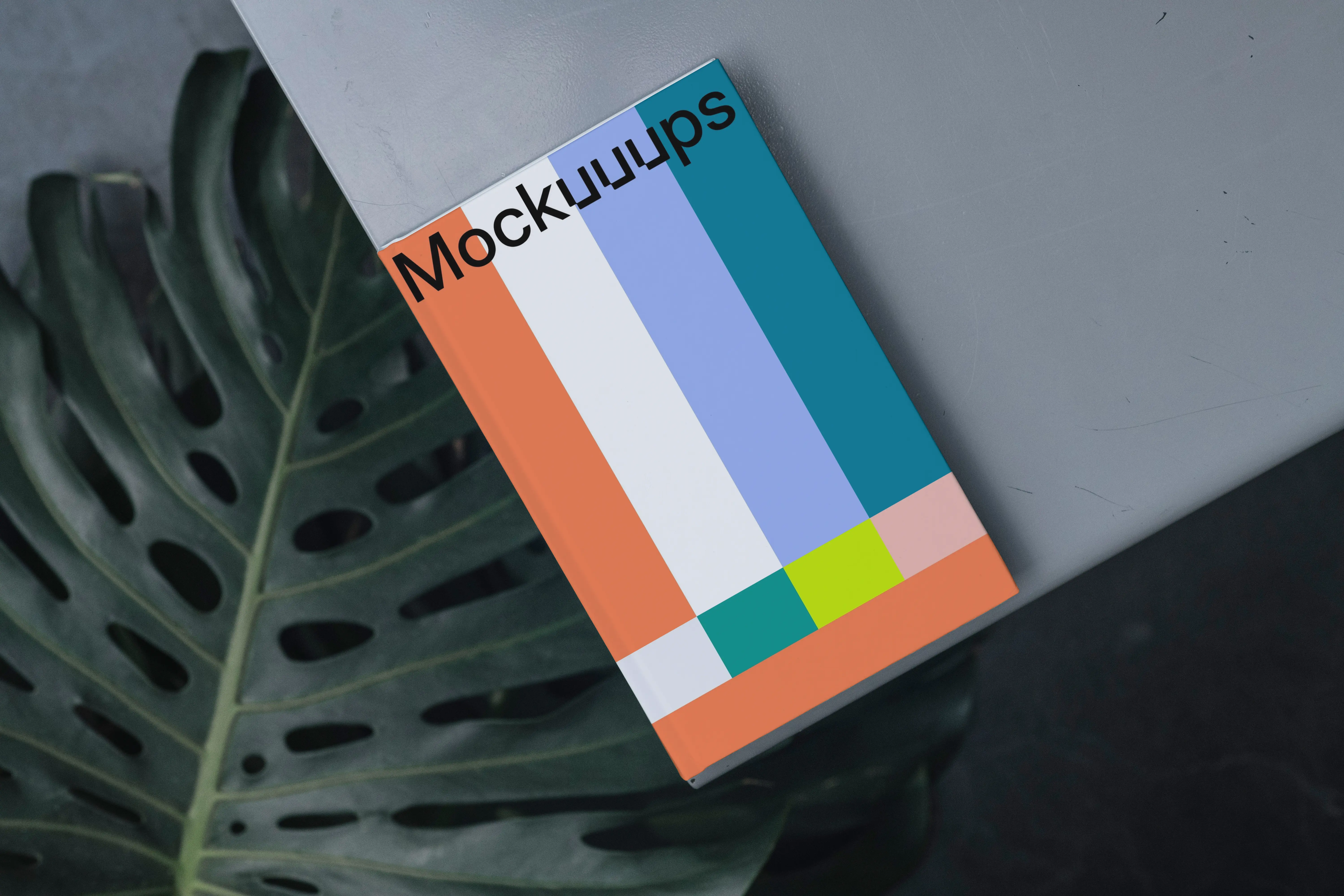 C-format book mockup on a gray surface with a tropical leaf