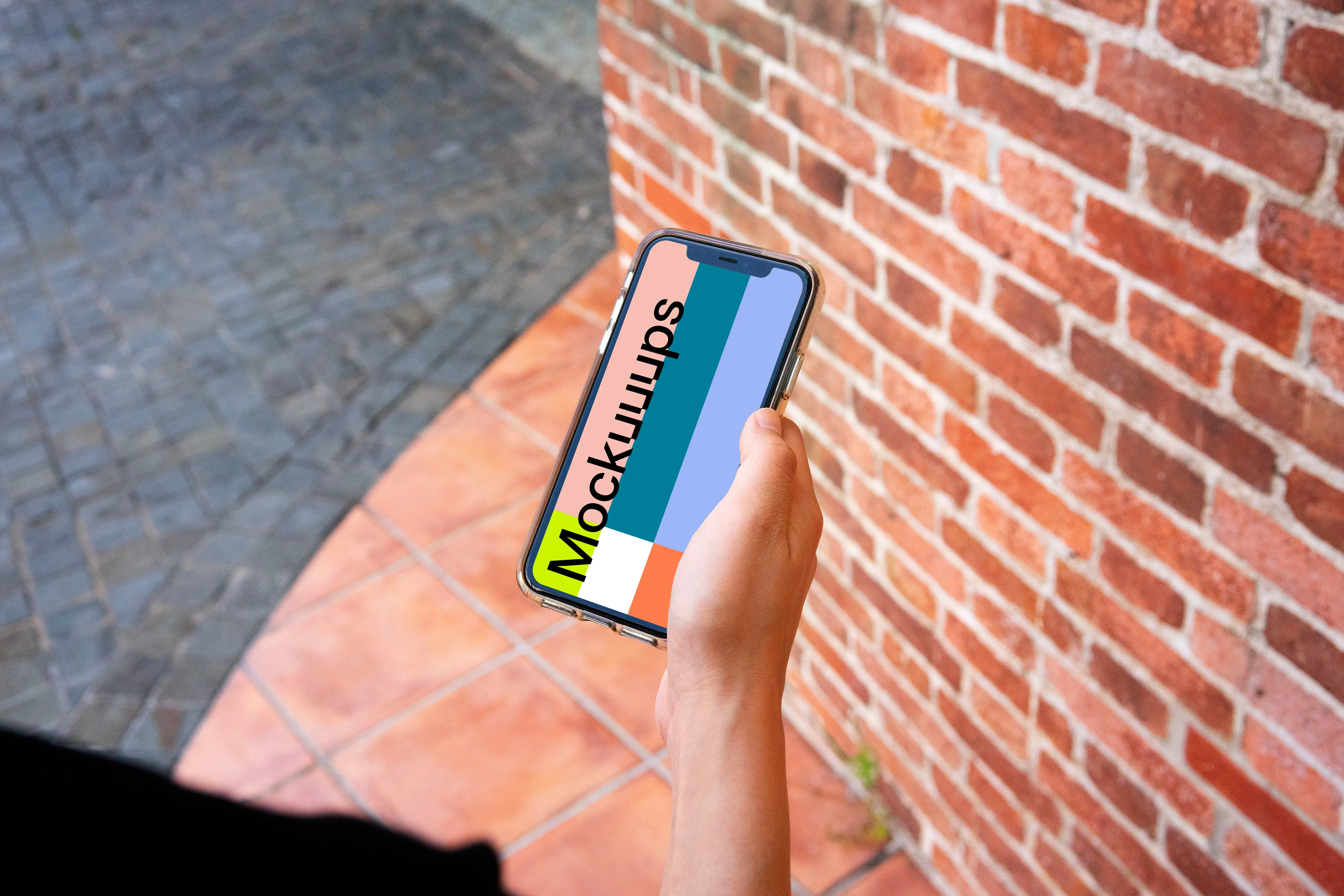 iPhone mockup held beside a brick wall