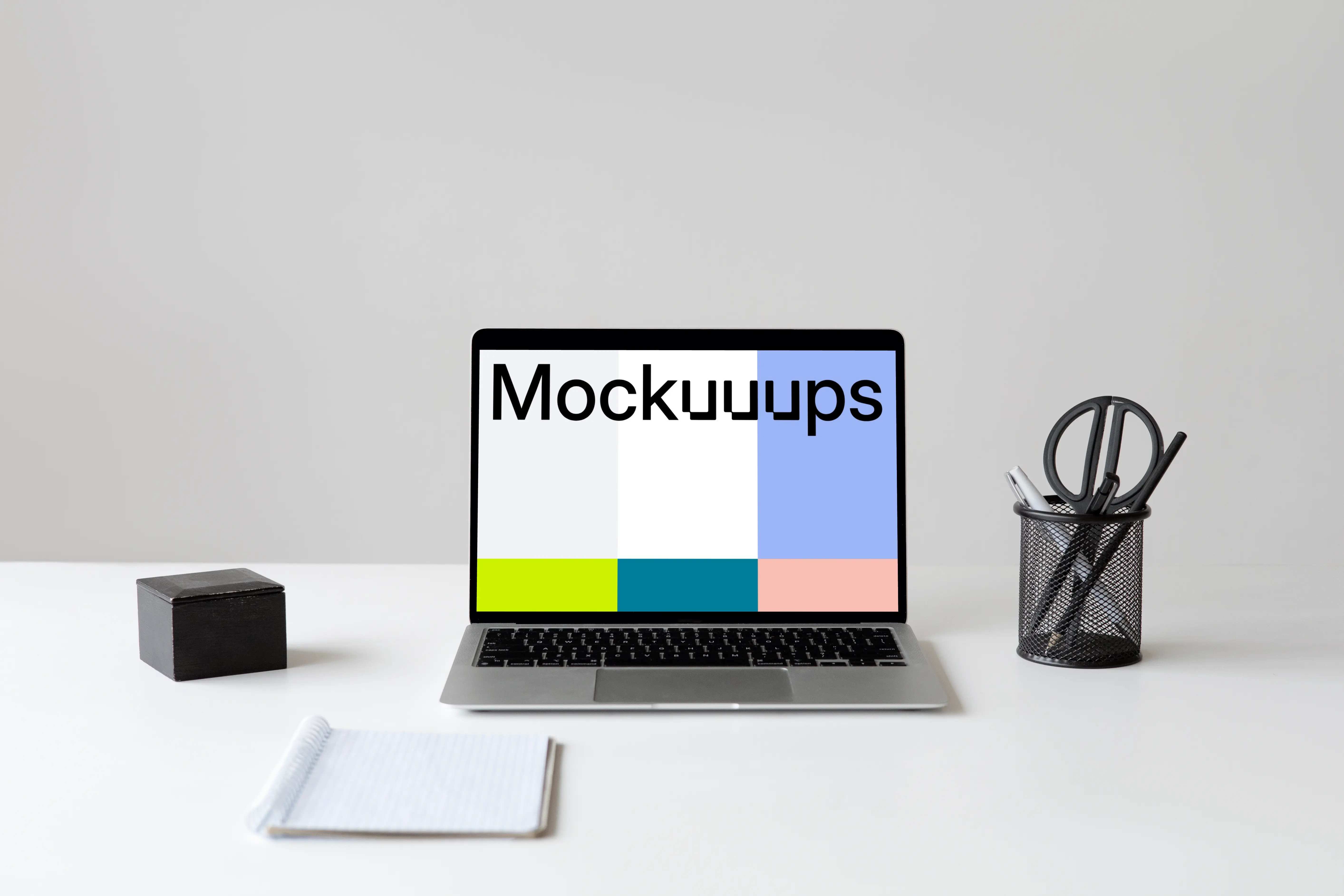 MacBook mockup on a white workstation table with cup of pens and scissors at the side