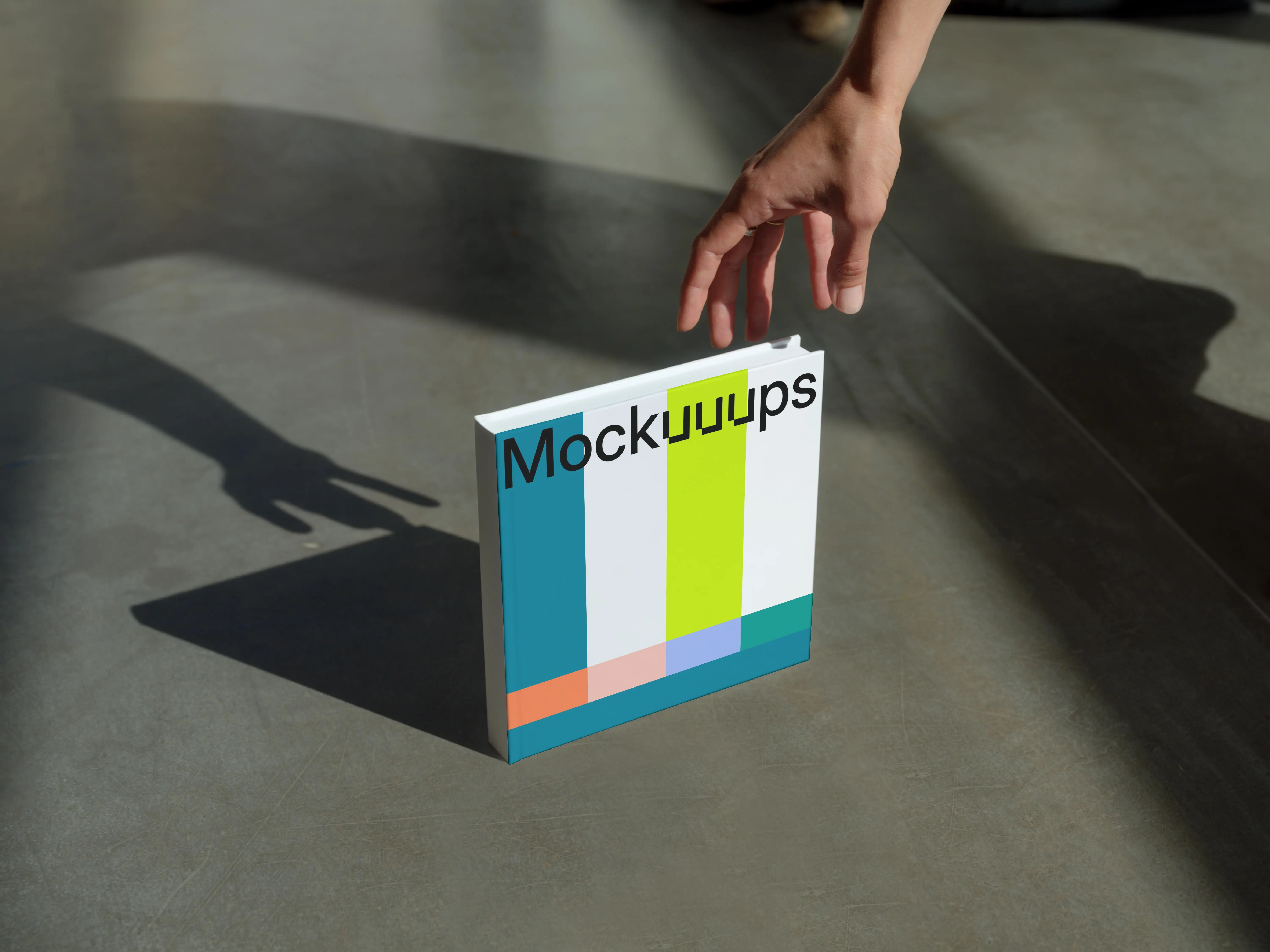 Mockup of a square book on a concrete surface with a hand reaching
