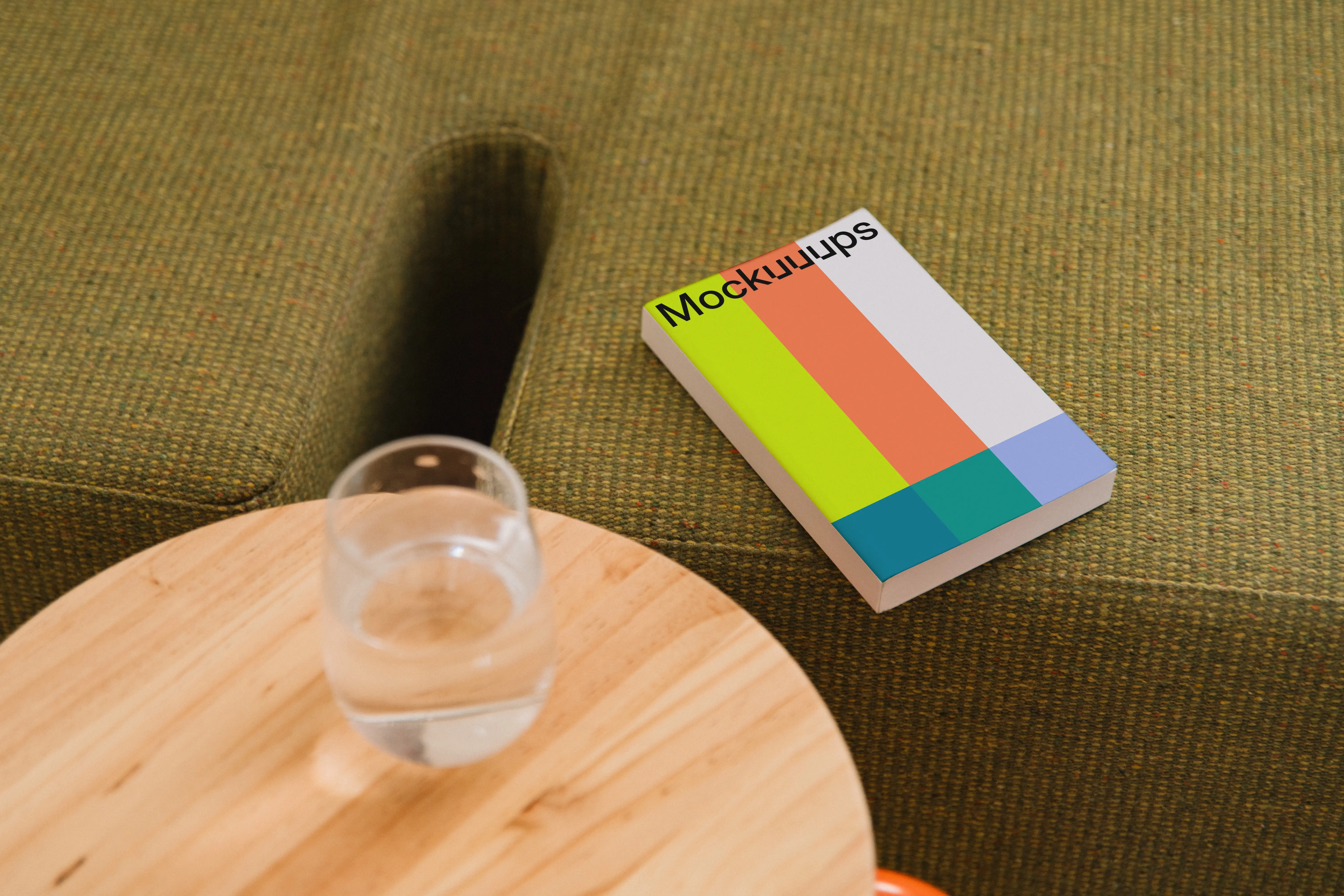 Paperback book mockup on a cozy green sofa