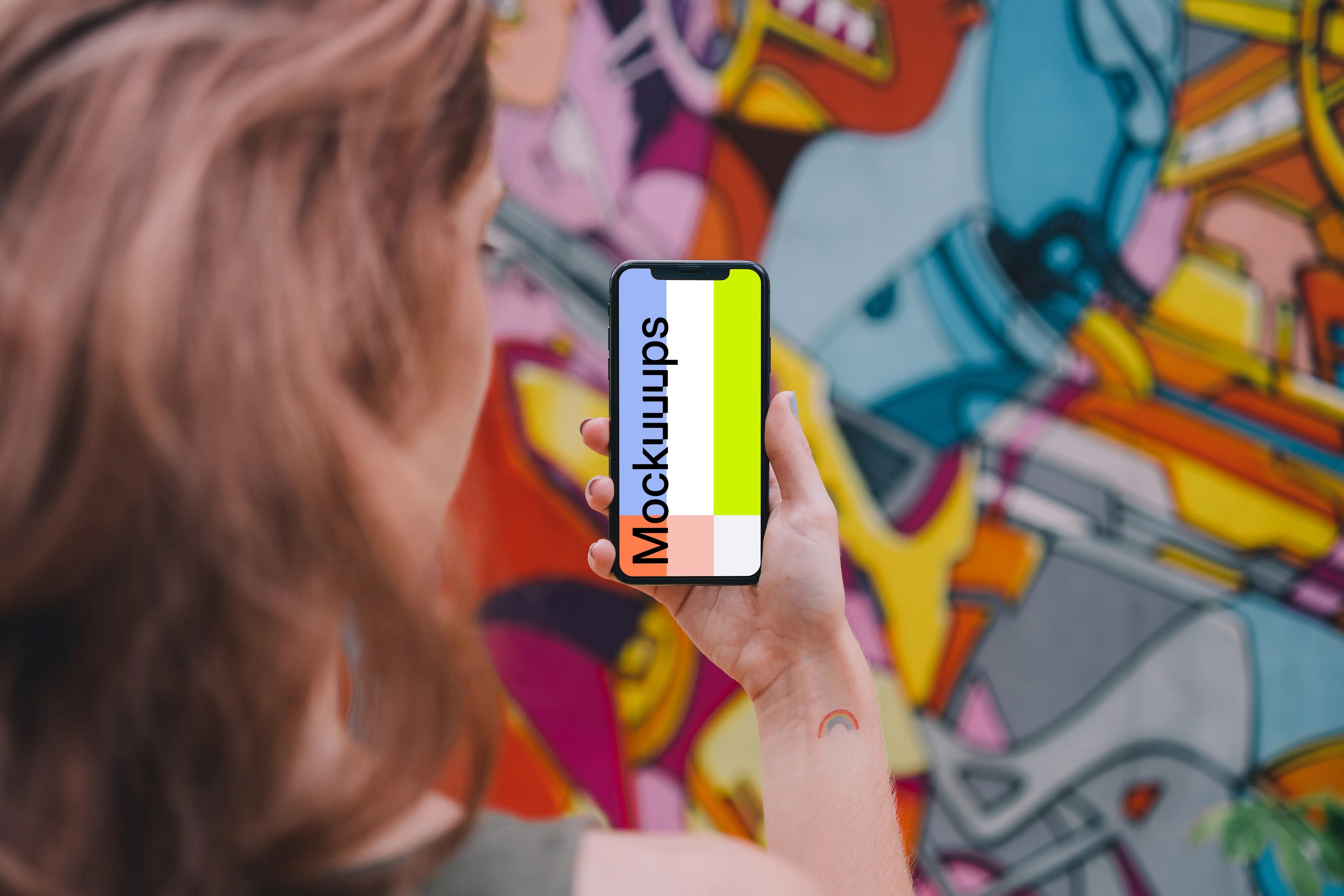 User holding iPhone in front of graffiti wall mockup